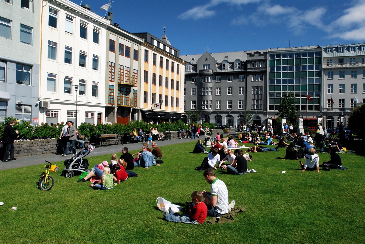 Mensen genieten van de zon op het grasveld bij Austurvollur in Reykjavik in het oude deel van het centrum.