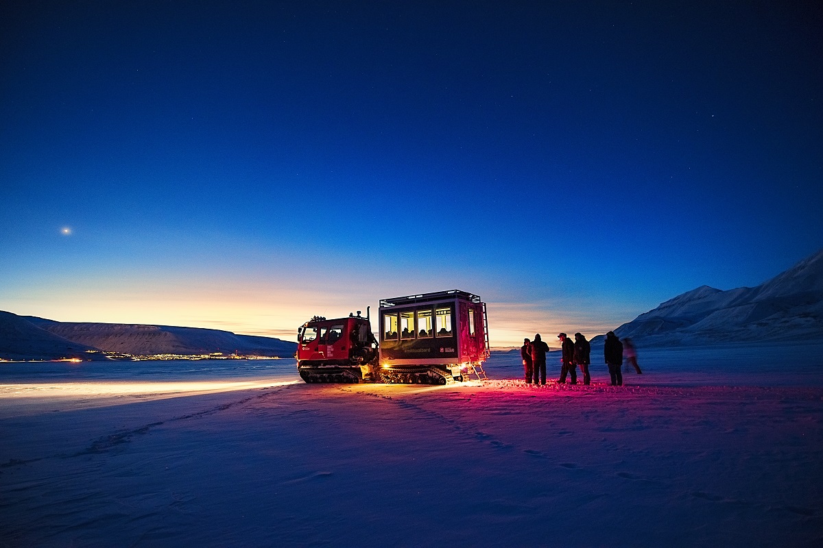 Reizigers staan naast een snowcat met Longyearbyen in Spitsbergen op de achtergrond.