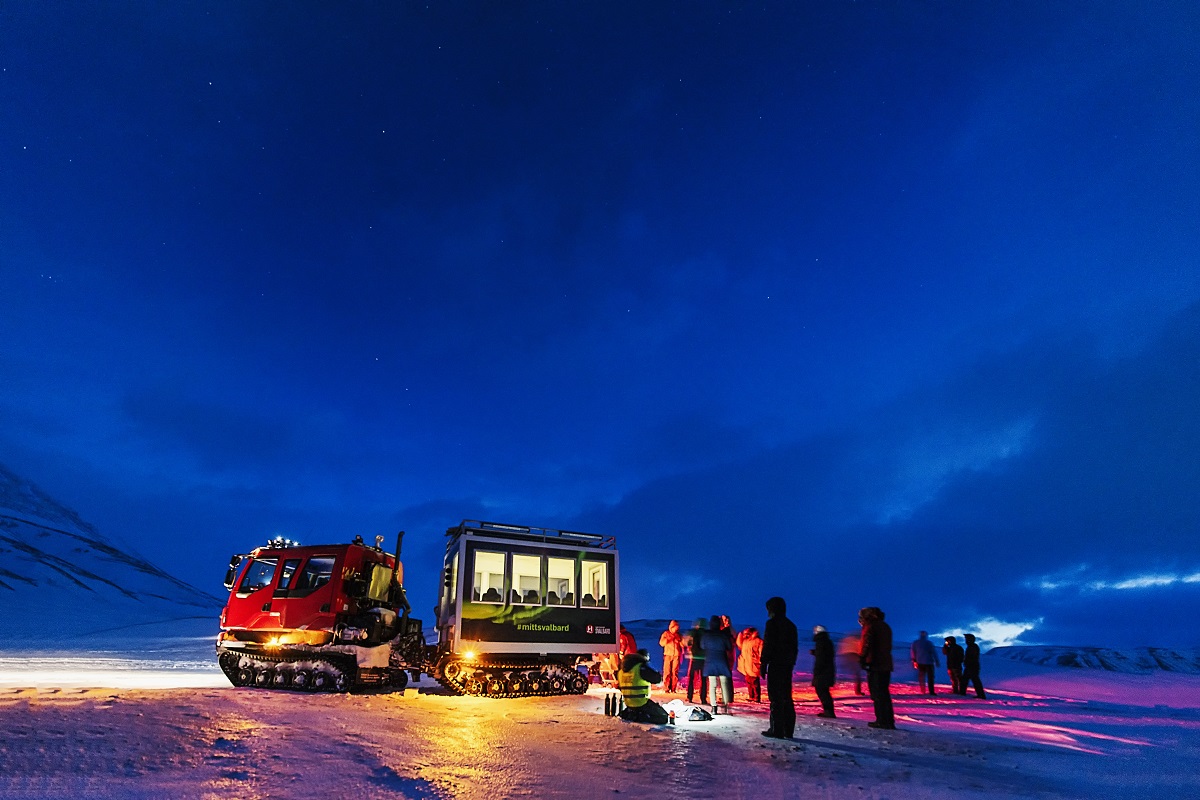 Een groep reizigers rond een snowcat tijdens een noorderlicht excursie in Spitsbergen.