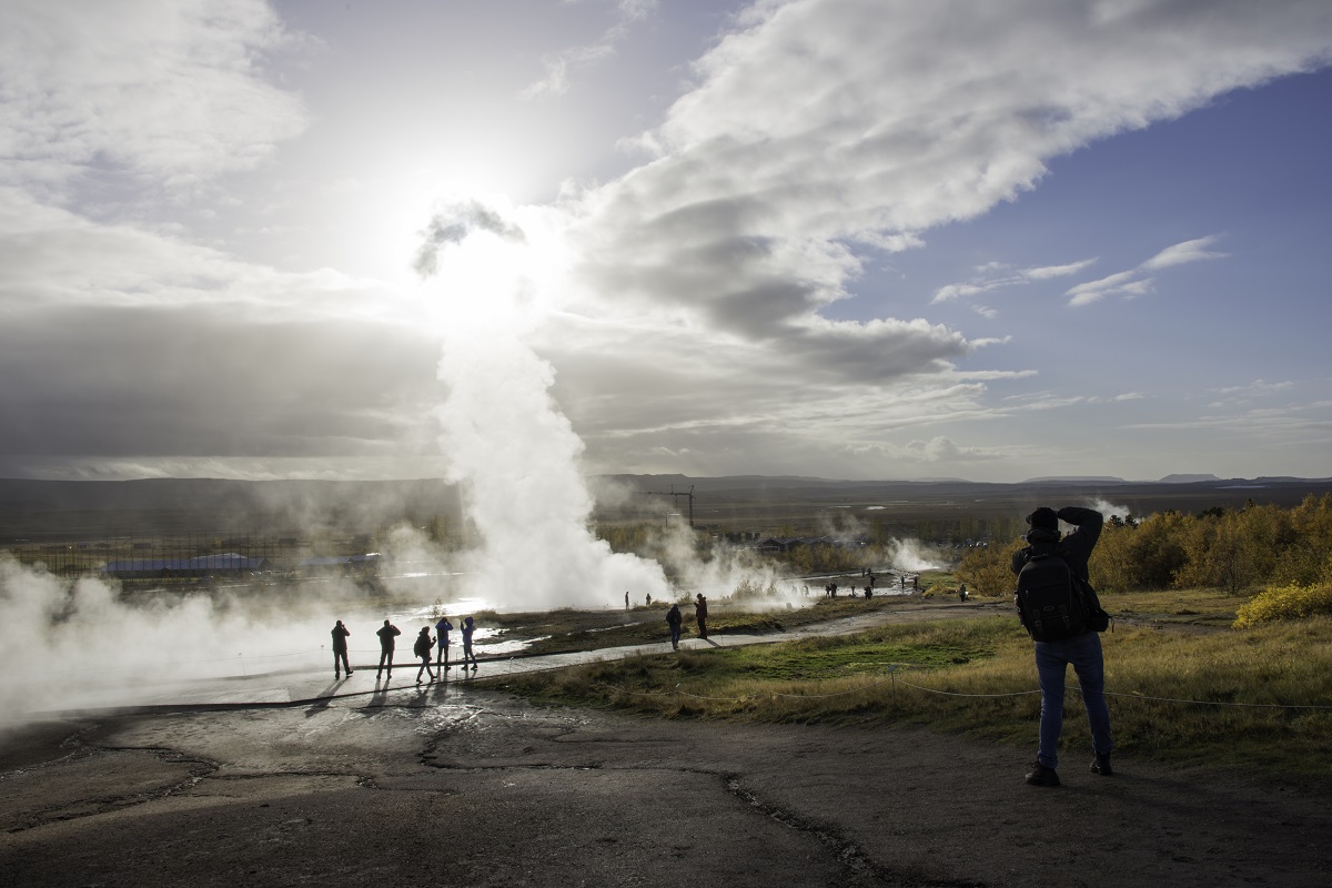 Een reiziger van FotoClass maakt een foto bij de geiser Strokkur in IJsland terwijl de zon door de stoomwolk probeert te breken.
