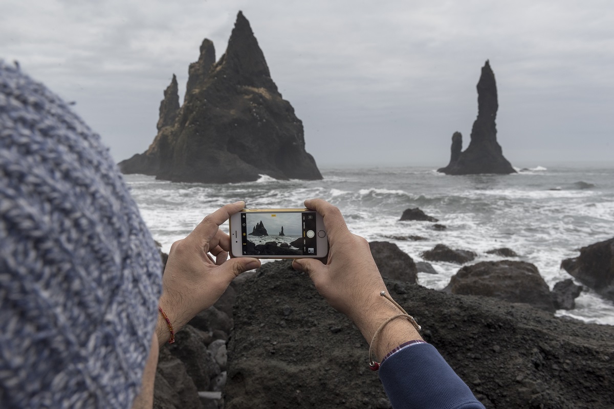 Een reiziger fotografeert op zijn telefoon de reynisdrangar rotsformaties in zuid IJsland.