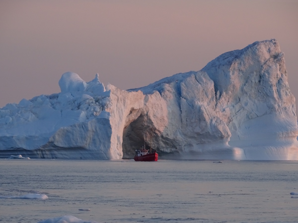Een bootje voor een enorme ijsberg tijdens een avond boottocht vanuit Ilulissat, West Groenland.