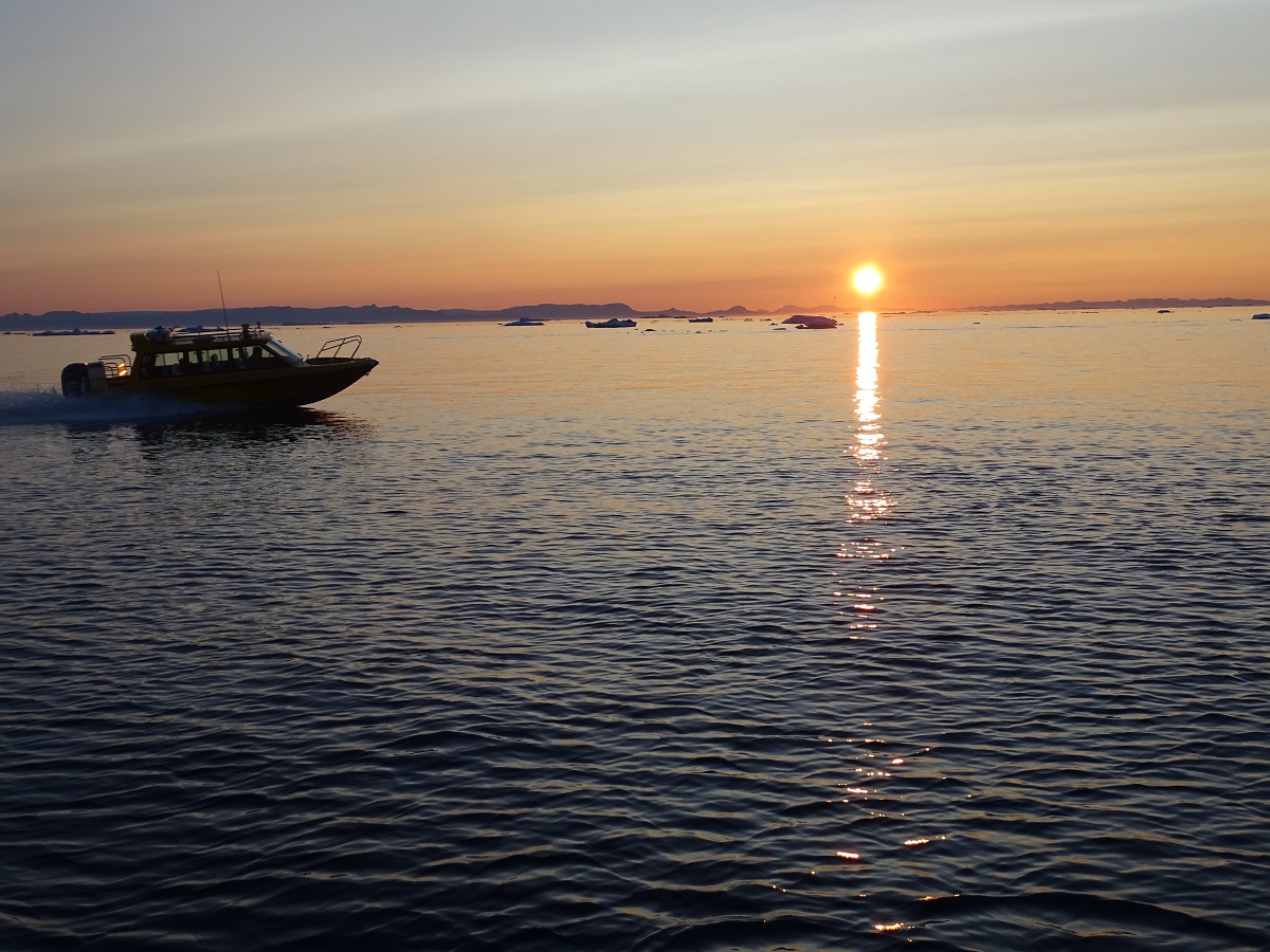 Een bootje vaart langs tijdens een avondcruise met de middernachtzon in Ilulissat, West Groenland.