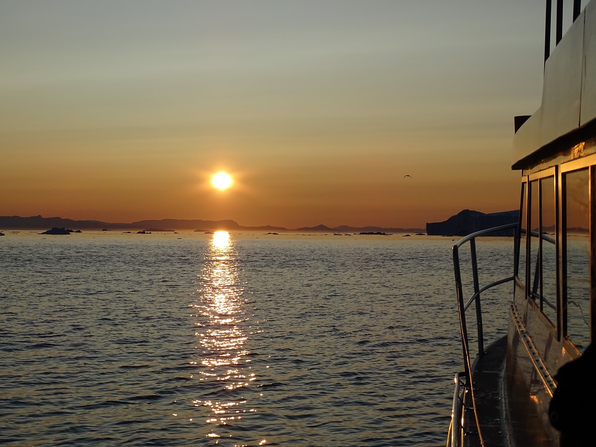 De laagstaande zon over het water gezien vanaf de boot op een avondcruise in Ilulissat, West Groenland.