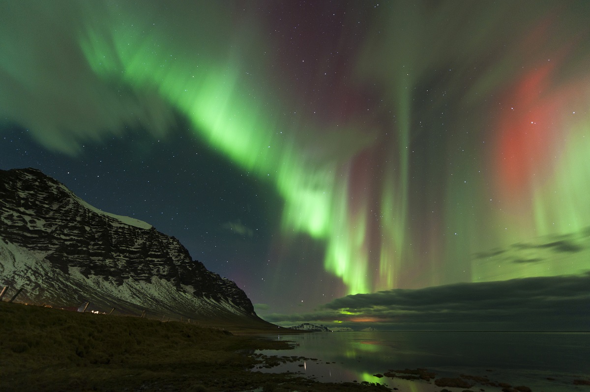 De Oostfjorden in IJsland in de winter met besneeuwde bergen en dansend noorderlicht, groen en rood gekleurd.