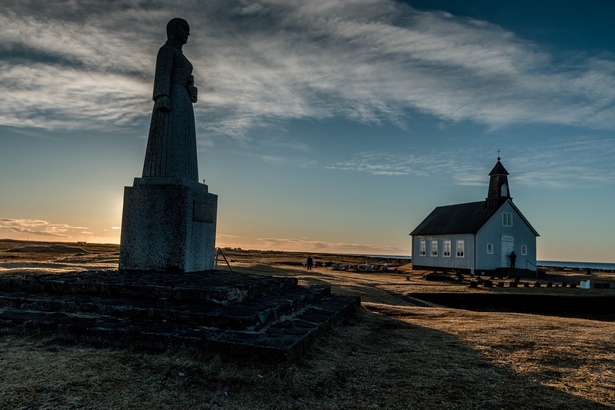 Standbeeld en kerkje bij ondergaande zon bij Strandakirkja op Reykjanes in IJsland.