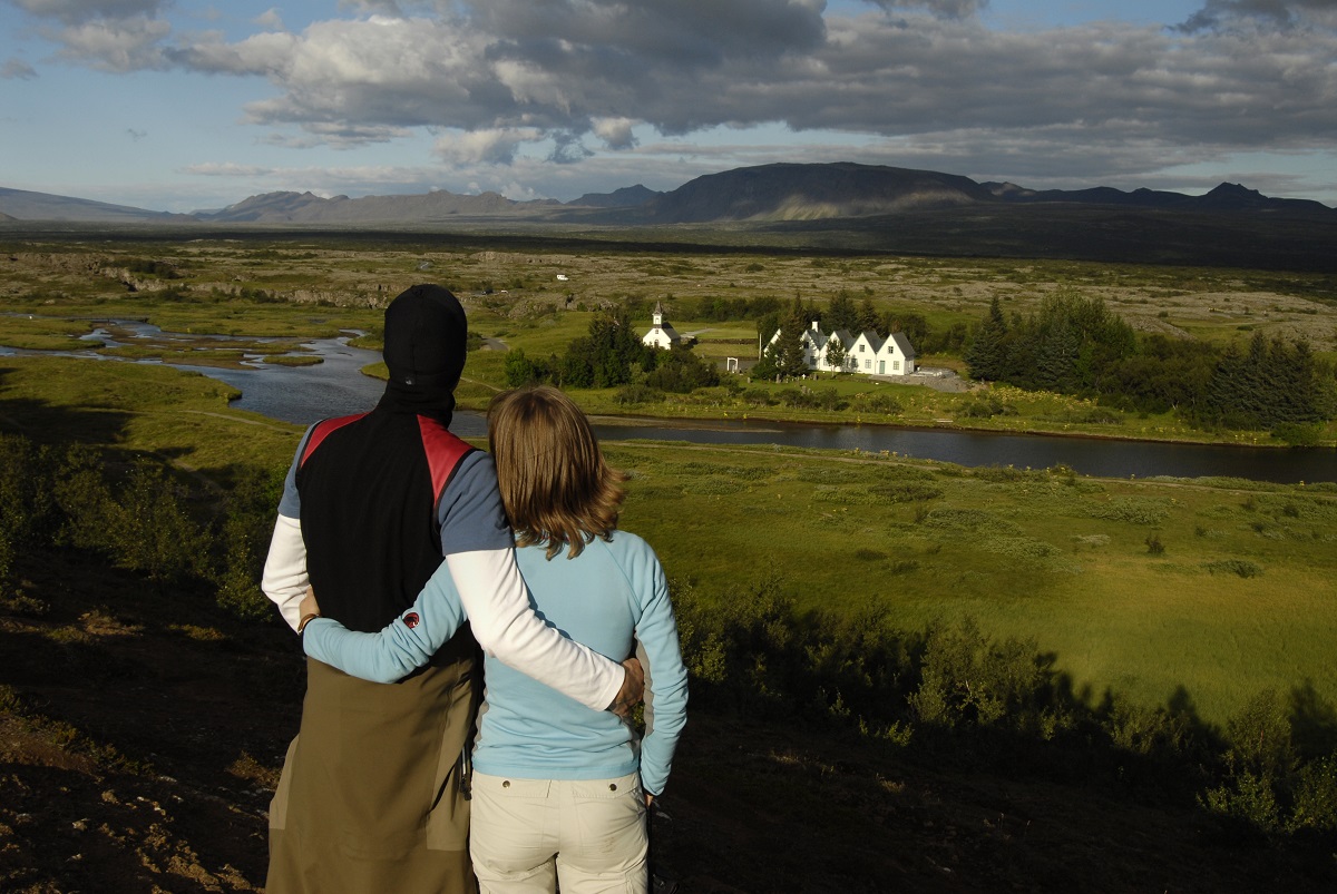 Een stel kijkt uit over de vallei Thingvellir in IJsland, met het witte kerkje uit 1859 op de achtergrond.