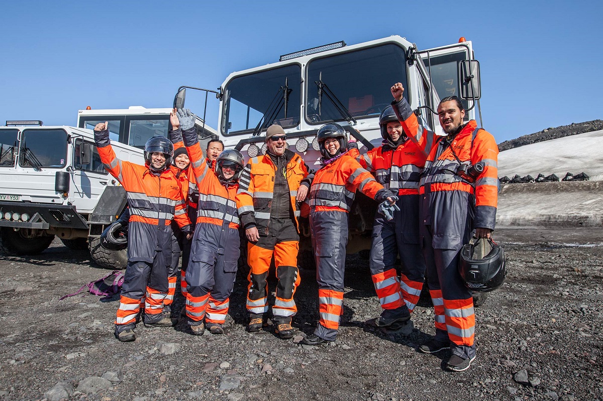 Deze groep toeristen staat klaar voor de sneeuwscootertocht bij de monstertruck op IJsland in oranje thermopakken.
