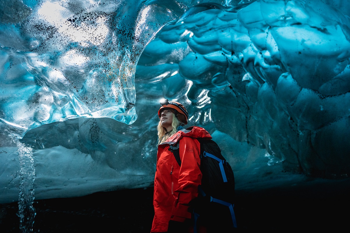 Een reiziger in een rode jas staat in een ijstunnel onder de Vatnajokull.