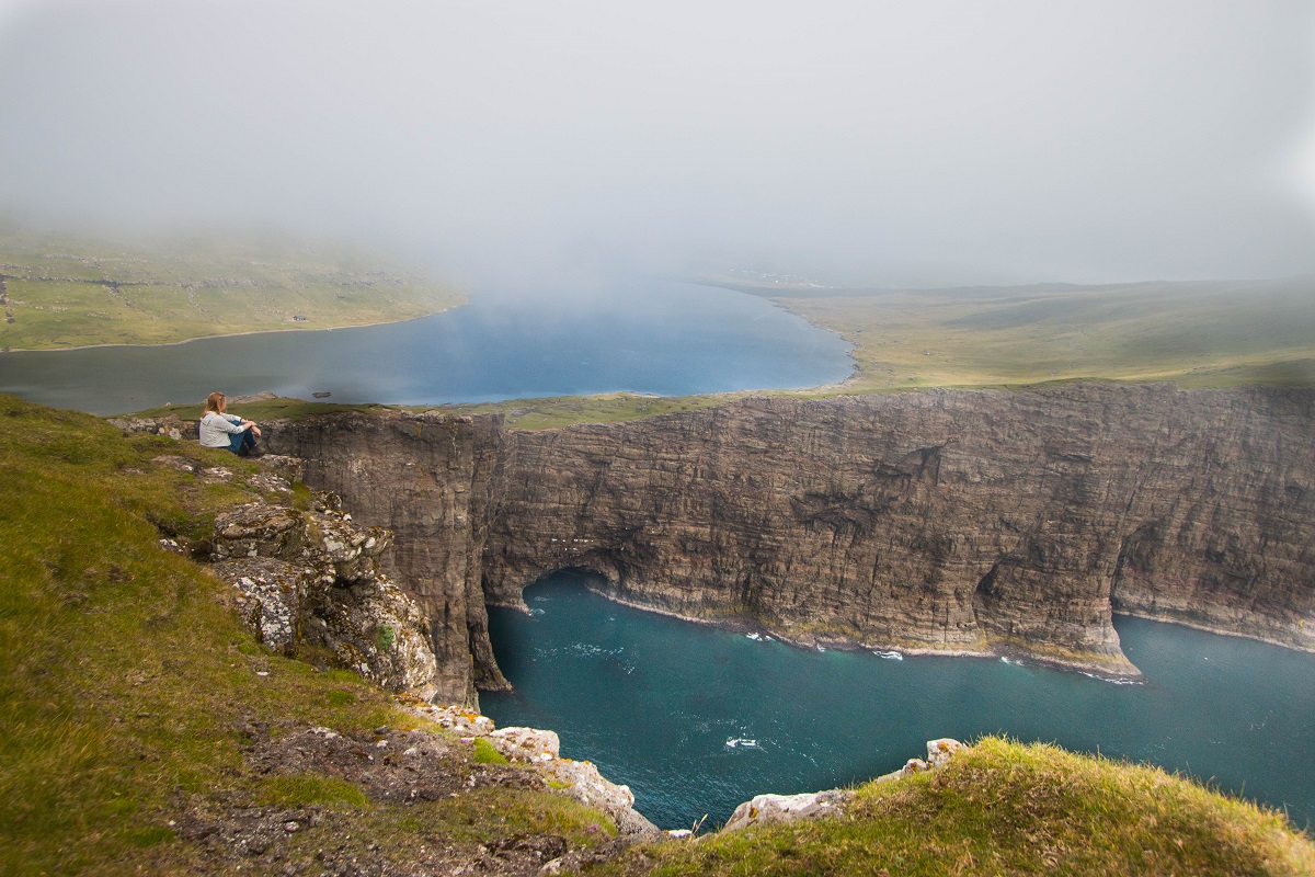 Wandelaar geniet van het uitzicht op de kliffen in de mist tussen twee meren op Vagar, Faroer.