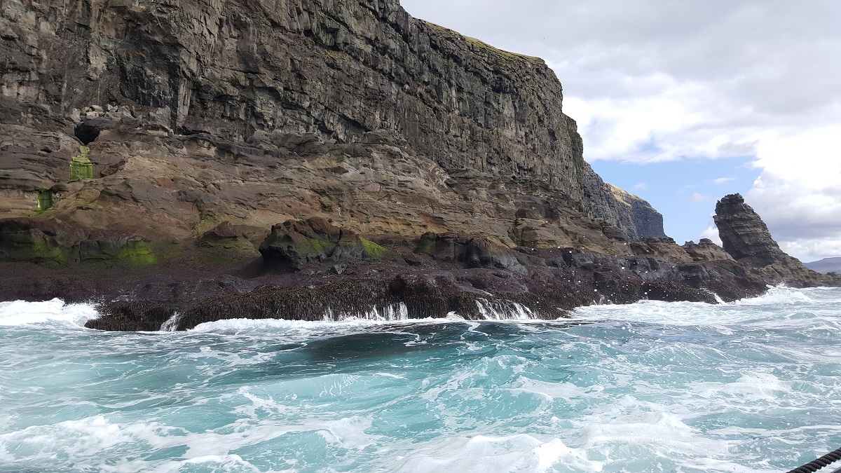 Het heldere zeewater klotst tegen de kliffen van Hestur bij de Faroer eilanden.