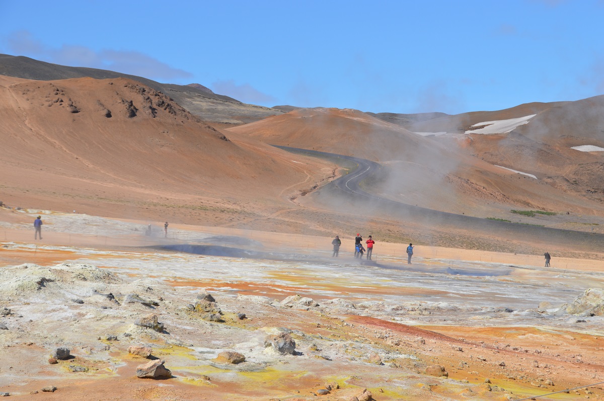 Mensen in een kleurrijk landschap, bij Namaskard in noord IJsland, met geothermische bronnen en een helder blauwe lucht.