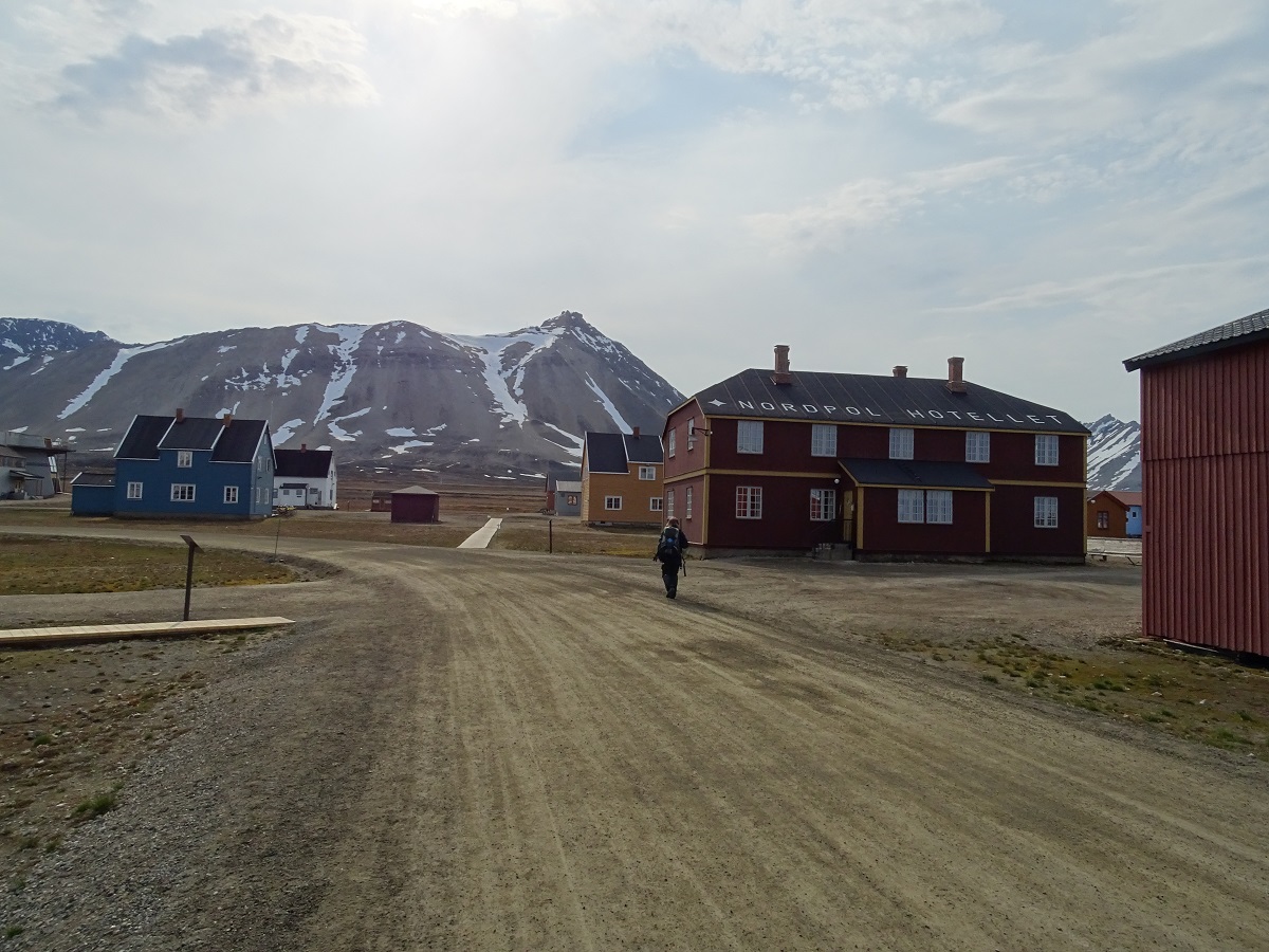 Wandelaar langs rode, gele en blauwe huizen en het Nordpol Hotellet in het dorpje Ny Alesund, Spitsbergen.