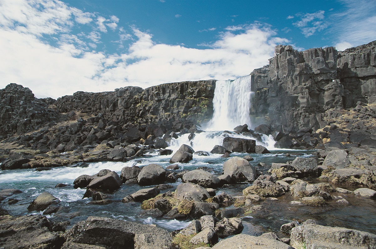 Mooie waterval, in NP Thingvellir in zuid IJsland, valt tussen basaltrotsen naar benenden met mooie wolkenlucht.