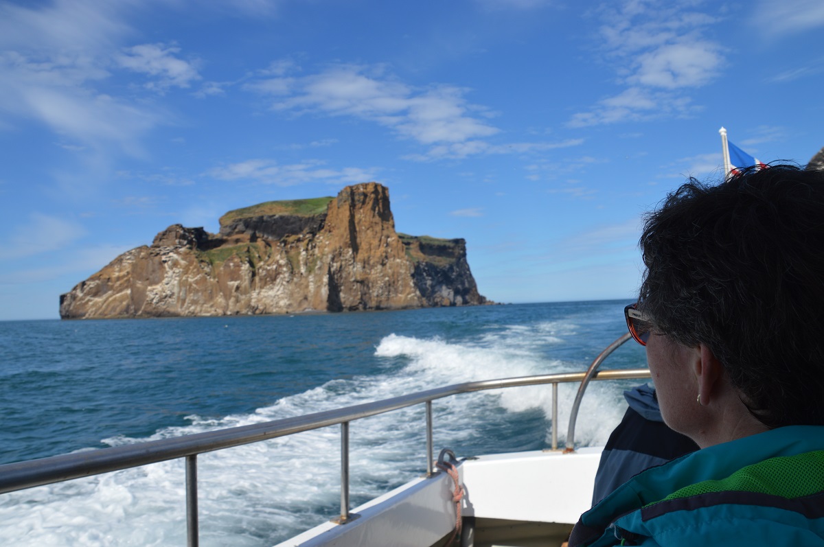 Een reiziger kijkt vanaf de boot naar het eiland Drangey, tijdens een excursie op IJsland.