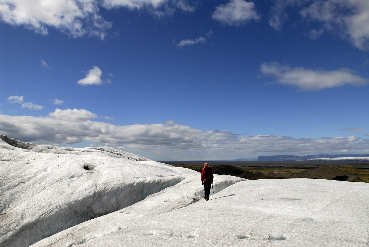 Een wandelaar loopt op de gletsjer Svinafellsjökull, IJsland, met een prachtig uitzicht en een heldere blauwe lucht.