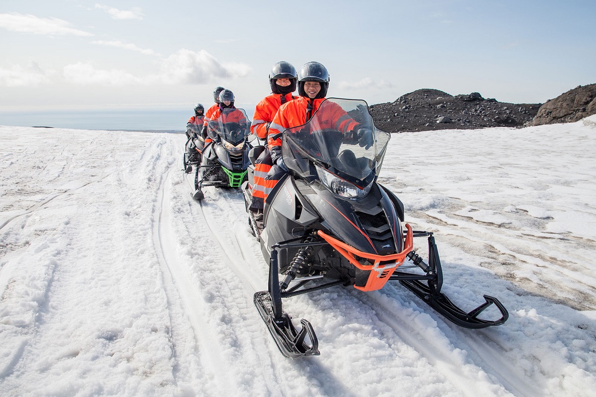 Een groep reizigers zit in tweetallen op de sneeuwscooters op de Solheimajokull gletsjer in IJsland.