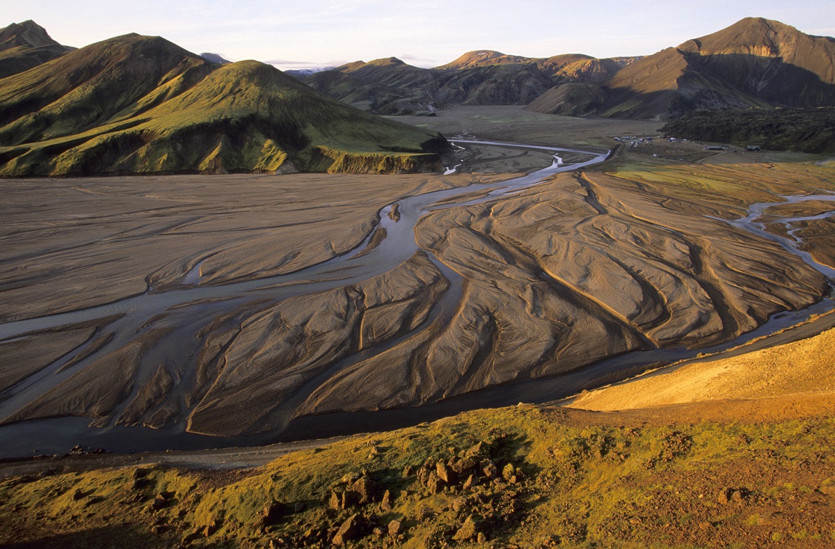 De rivier stroomt door de vallei bij Landmannalaugar, in de IJslandse hooglanden, langs geel en groene bergtoppen.