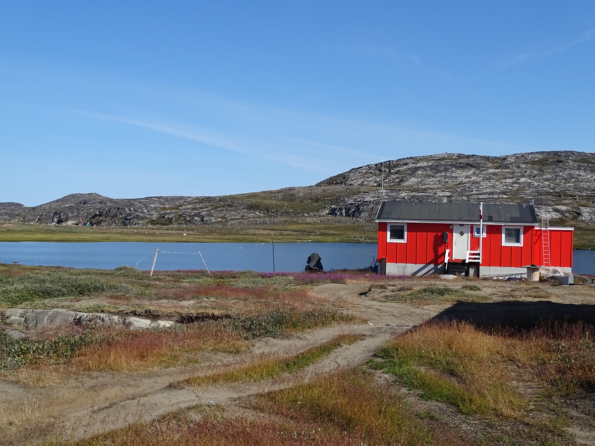 Rood houten huisje in Ilimanaq, west Groenland, met helder blauwe lucht en een mooi landschap.
