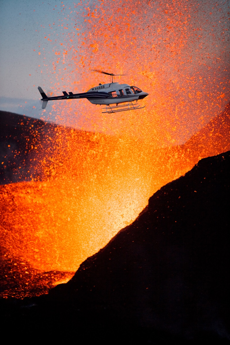Een helikopter vliegt langs de oranje, spuwende lava tijdens een vulkaanuitbarsting op IJsland.