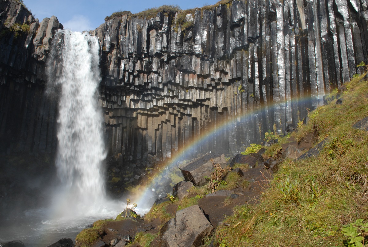 De Svartifoss waterval in Skaftafell met regenboog valt tussen de basaltrotsen naar beneden.