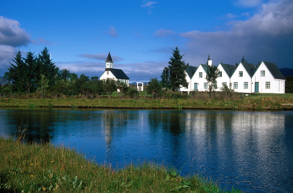 Witte kerk en huisjes aan het blauwe meer met mooie wolkenlucht in NP Thingvellir.