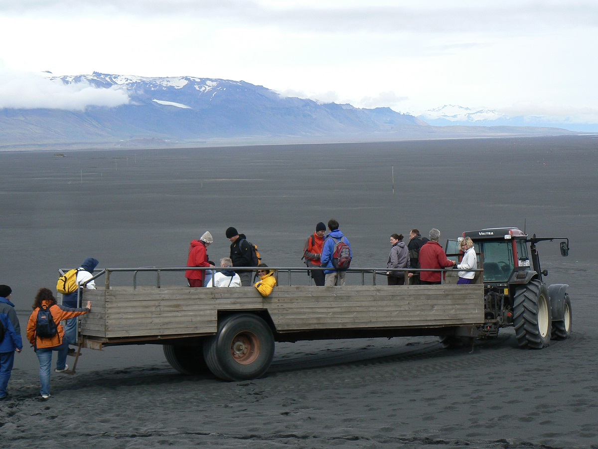 Reizigers stappen in de hooiwagen in een zwart lava landschap richting Ingolfshöfi in zuid oost IJsland.