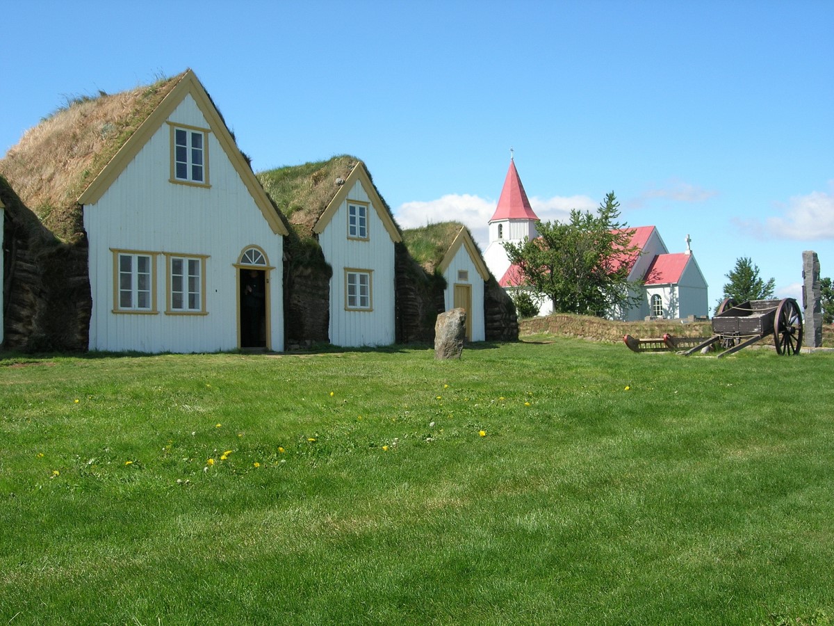 Een turfboerderij met mos bedekte daken en een wit met rood kerkje in Glaumbaer, noord IJsland, wat nu dient als museum.