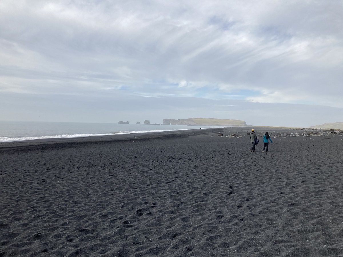 Toeristen lopen over het zwarte strand, Reynisfjara, bij Vik.