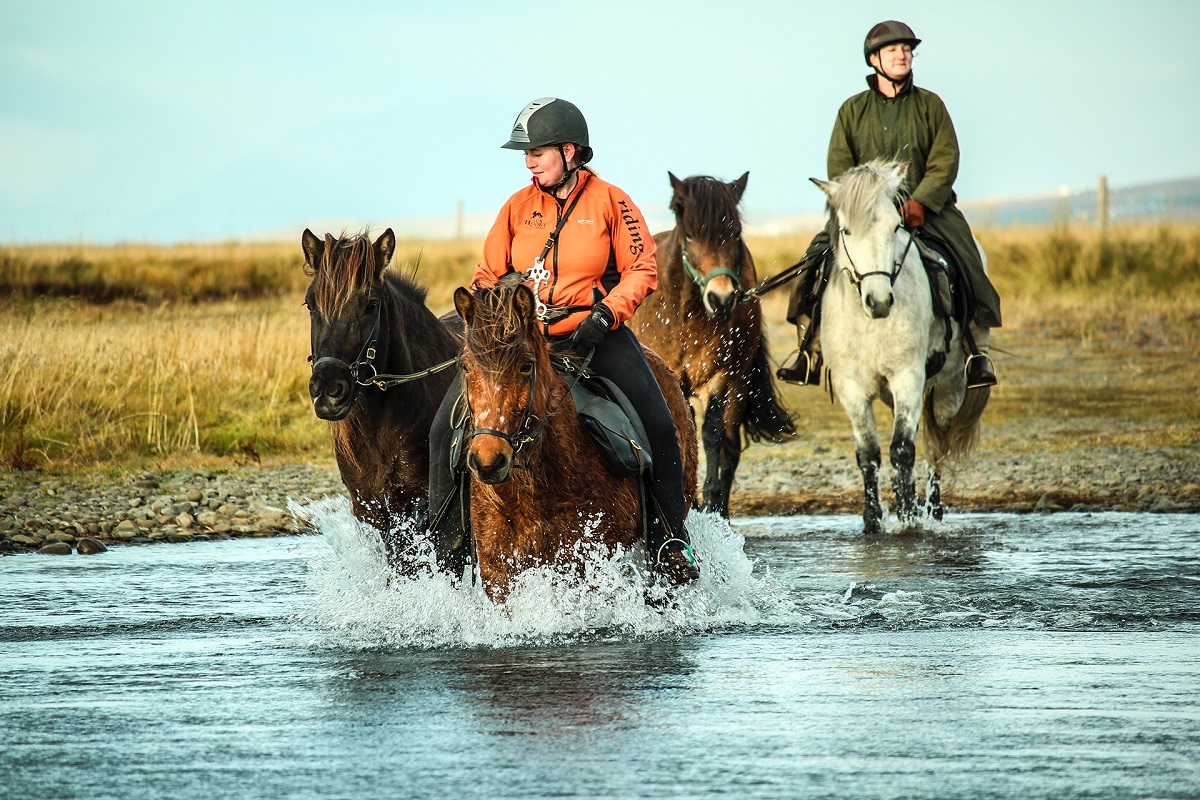 Twee ruiters en vier paarden doorkruizen een rivier.