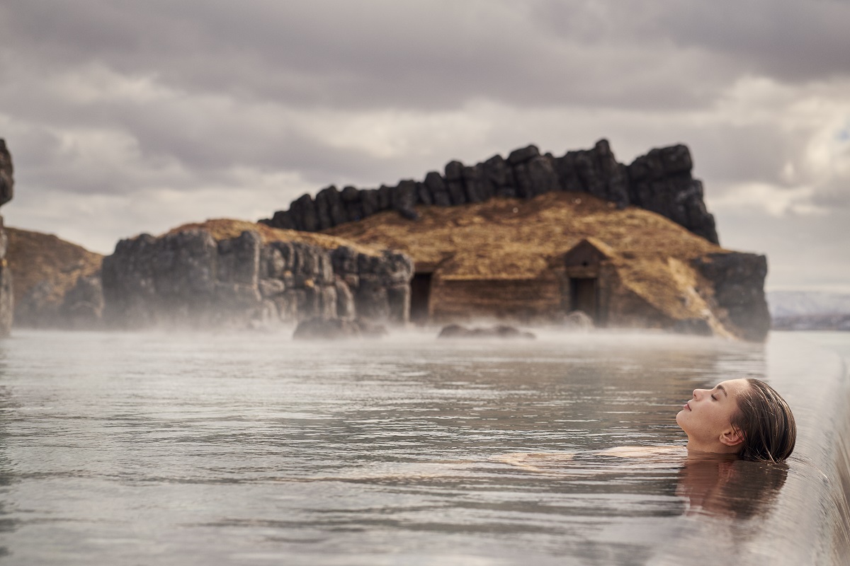 Een vrouw ligt te genieten aan de rand van het bad in de Sky Lagoon.