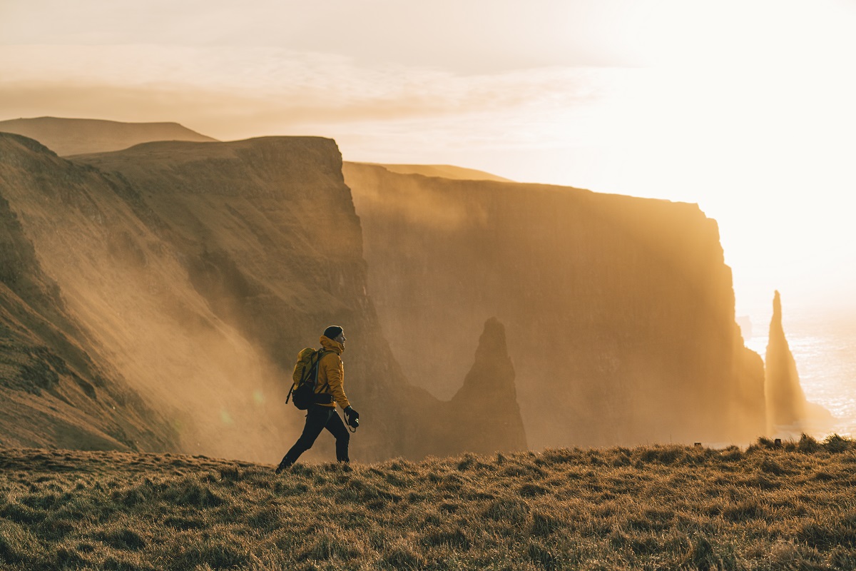 Een wandelaar wandeld langs de Faroese kliffen met zonsondergang en heeft prachtig uitzicht over de zee.