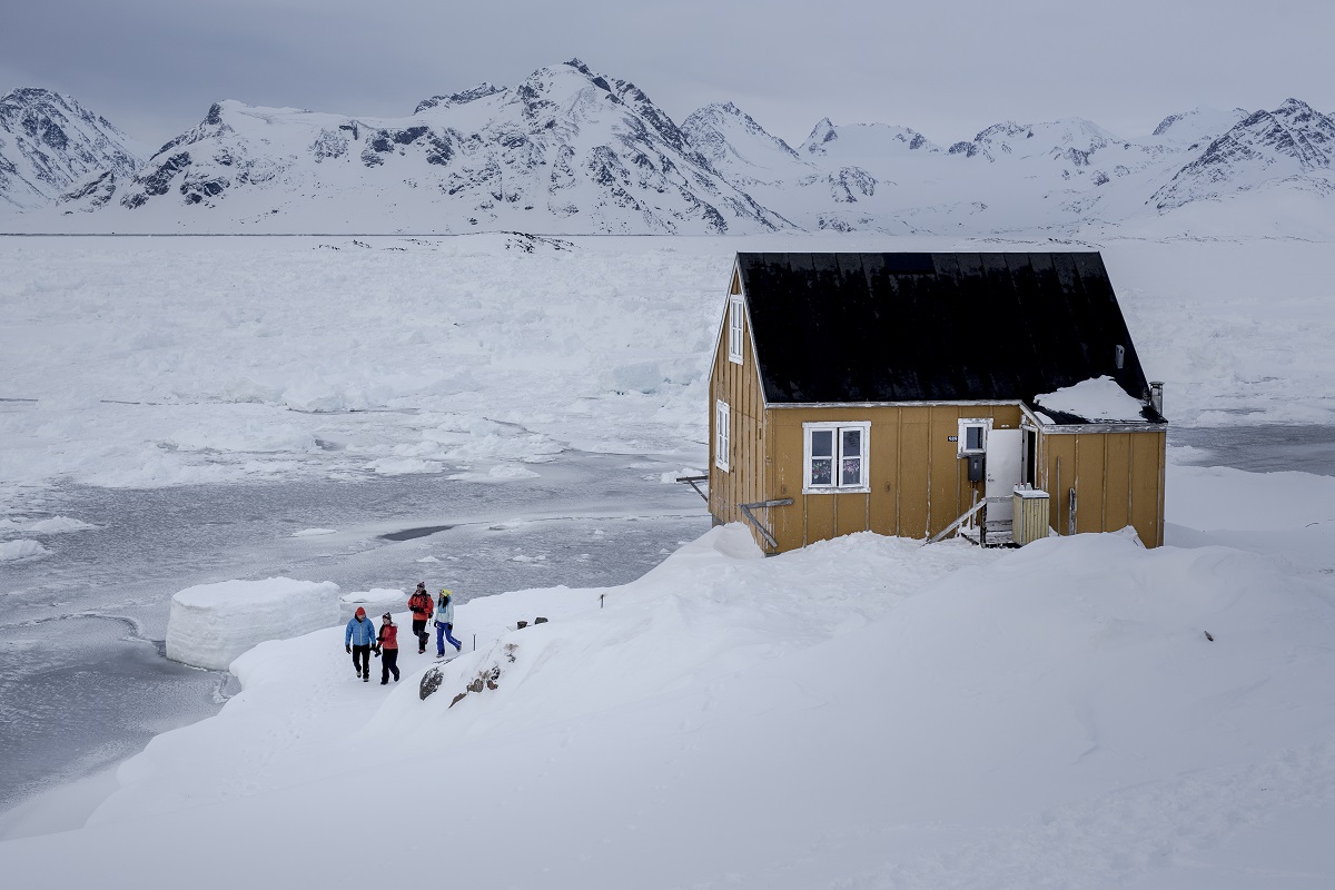 Groep mensen loopt langs een huisje op Groenland.