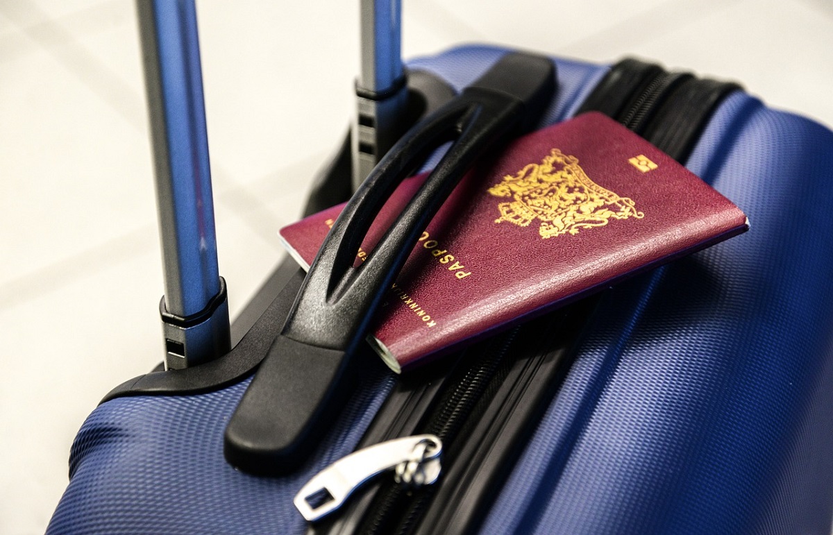 Een Nederlands paspoort gestoken onder het handvat van een rolkoffer.