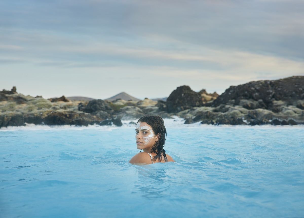 Een vrouw baddert in de Blue Lagoon, een warmwaterbron in Reykjanes IJsland en heeft een klei masker op haar gezicht.