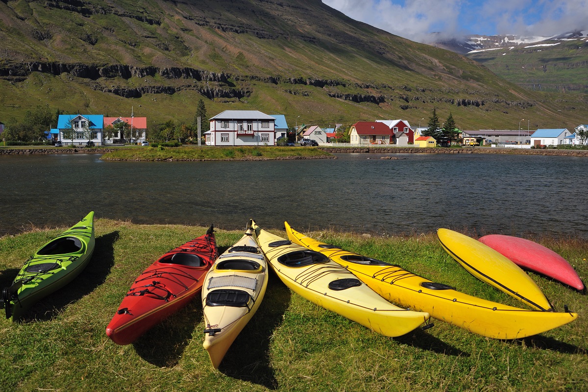 Zeven kleurrijke kajaks liggen op de rand van de fjord in het zicht van een dorpje.
